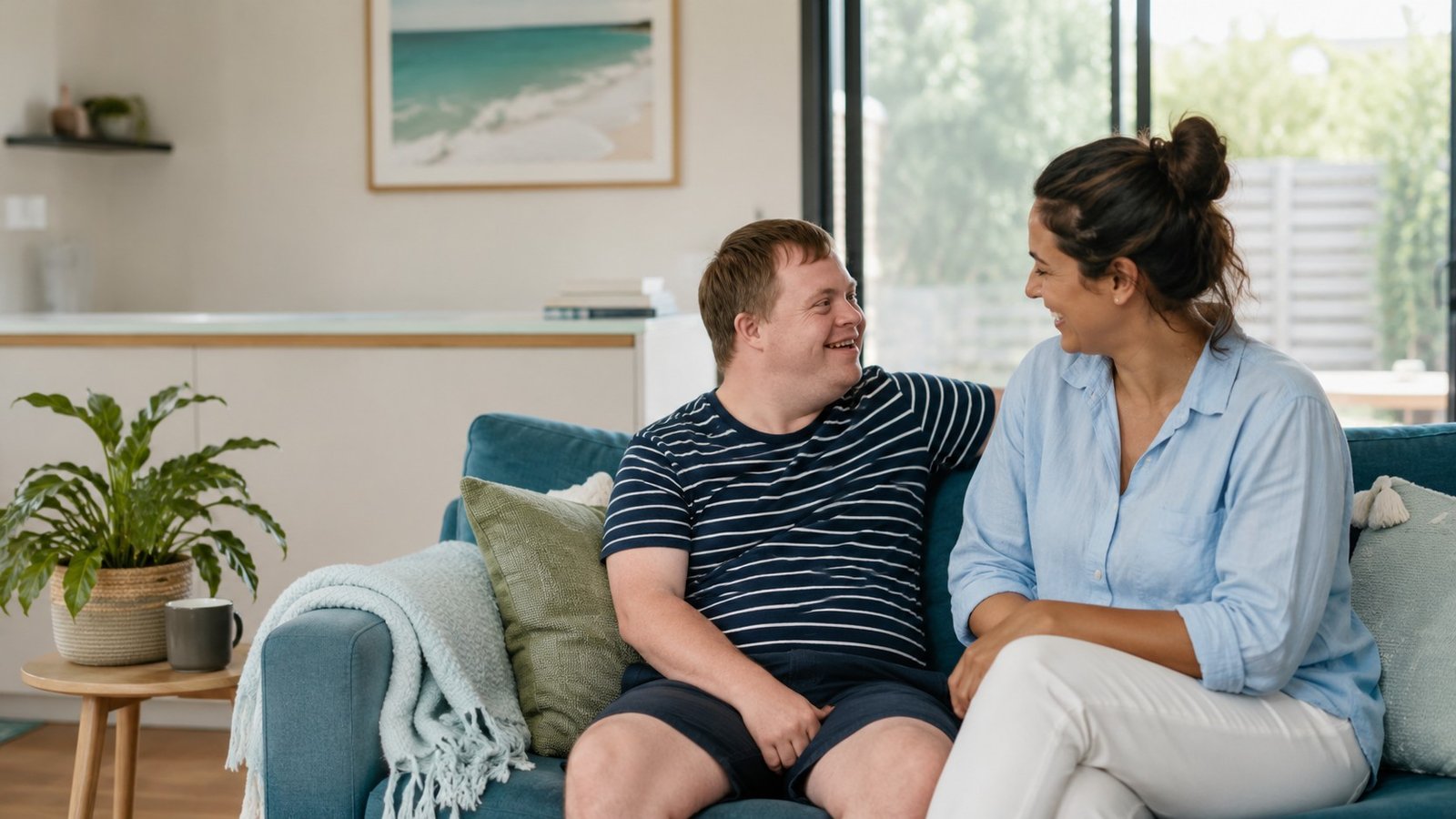 A relaxed one-to-one moment between a support worker and a young person chatting on a couch at home