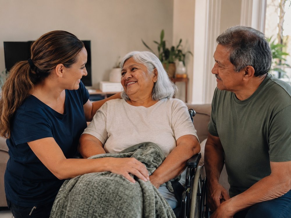 A support worker and a family member sitting warmly with an older woman using a wheelchair at home